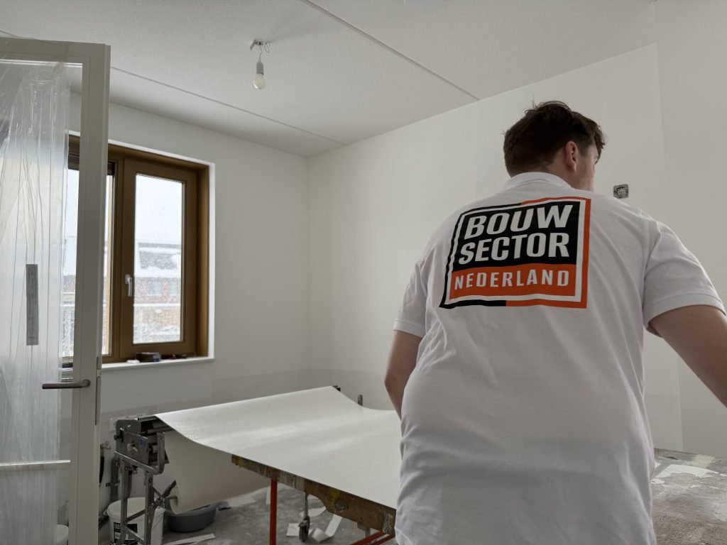Behanger van Bouwsector Nederland in bedrijfsshirt bij de plaktafel in een lege nieuwbouwkamer