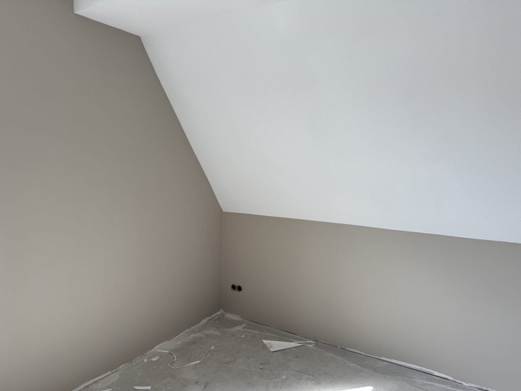Zolderkamer in een nieuwbouwwoning met een schuine wand en kale wanden, klaar voor de afwerking